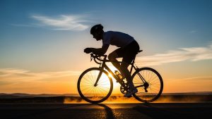 This is an image of a cyclists silhouette with the sun setting in the background and steam coming off the pavement. This type of vitality is the result of quality functional medicine.