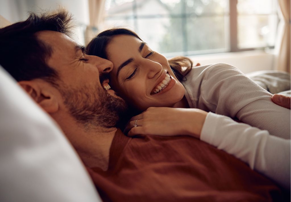a woman lays smiling on the chest of her happy husband. we see a ring on her wedding finger and they are relaxed and in love thanks to erectile dysfunction Tampa treatments.