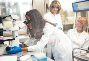 a group of female scientists work in a lab around a microscope to ensure dosing accuracy. this will help minimize progesterone side effects for patients.